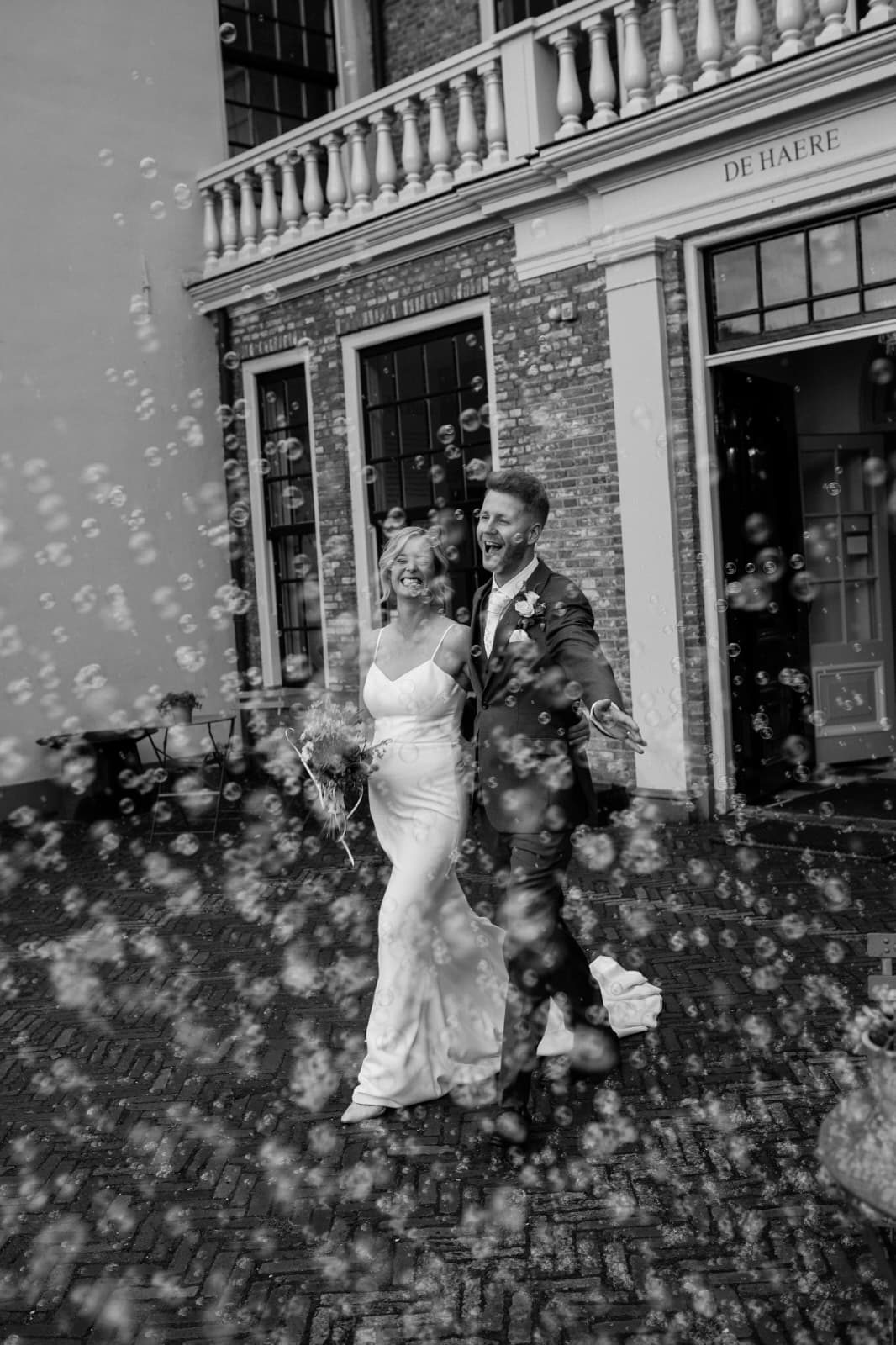 Bruidspaar loopt lachend door een regen van confetti voor het landhuis